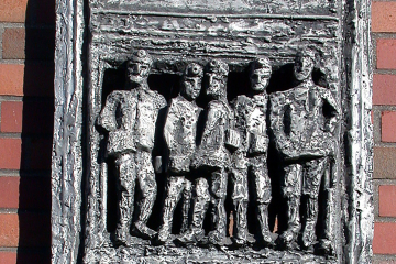 Das Aluminiumrelief zeigt einen zweietagigen Förderkorb, in dem Bergleute stehen.